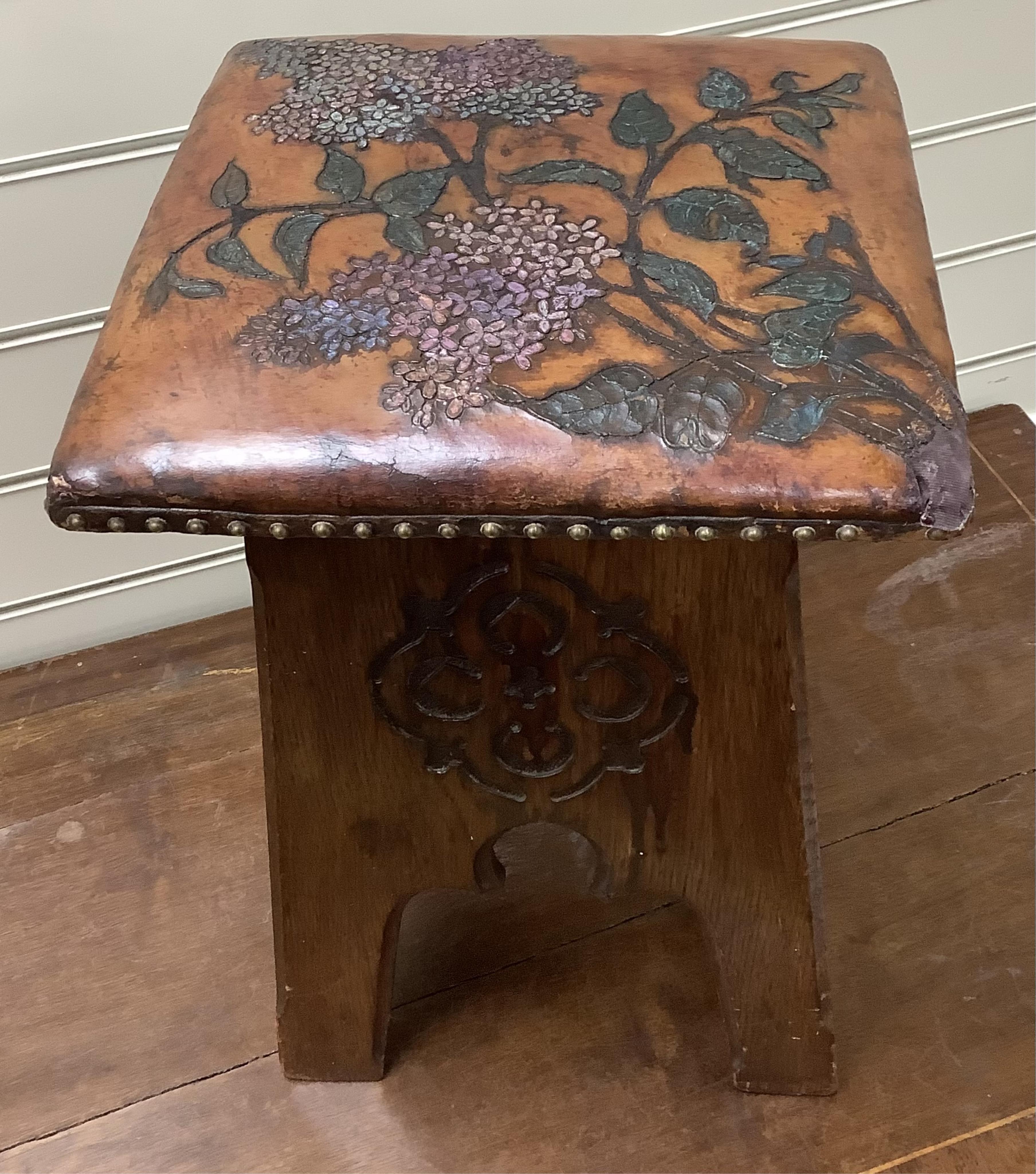 An early 20th century Liberty & Co. Arts & Crafts style stool with embossed leather seat, (later coloured), width 31cm, height 42cm. Condition - fair